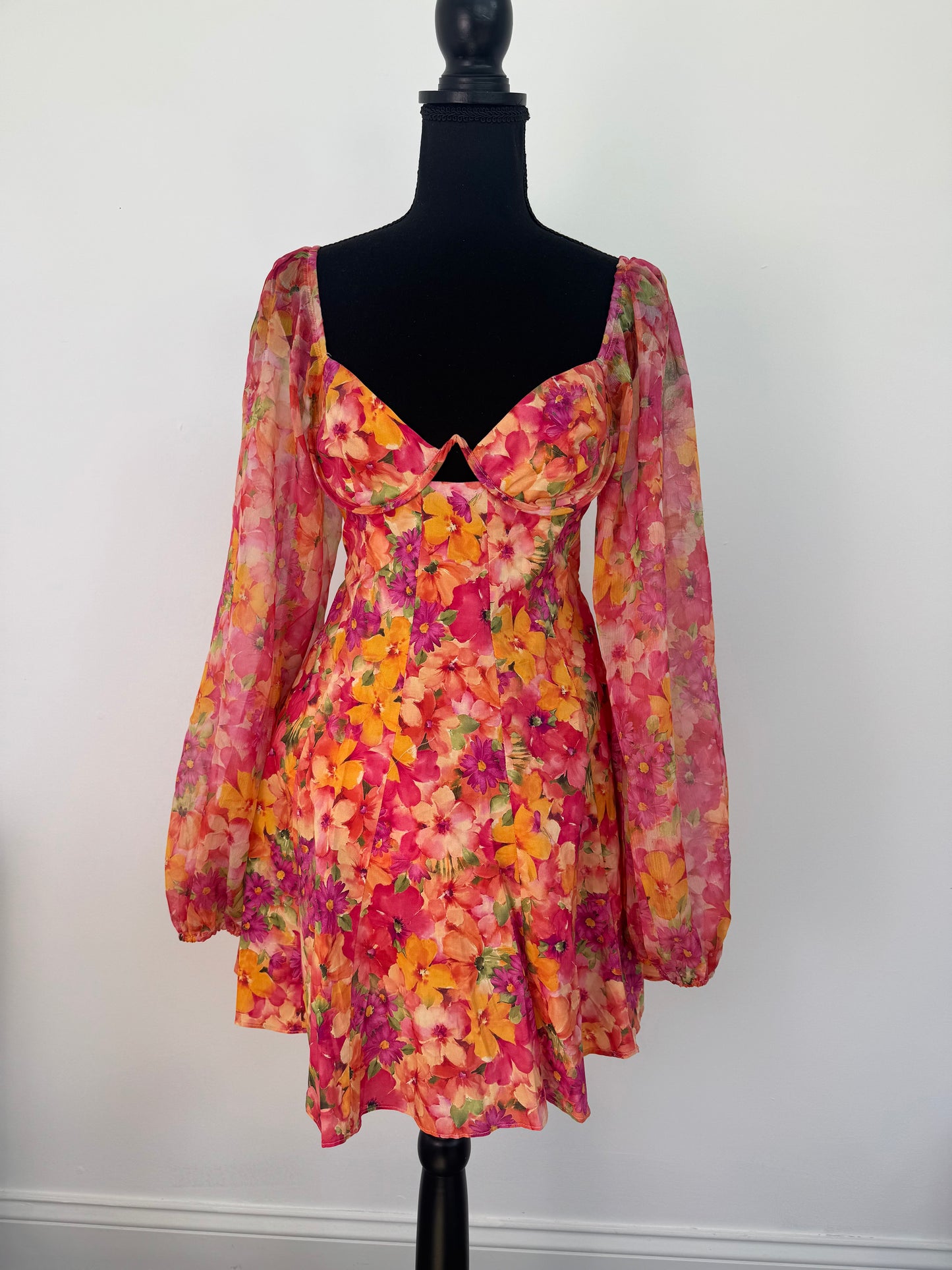 View of front of dress. Orange and pink tropical flower design with hardware bust, sheer sleeves with tropical flower design. 